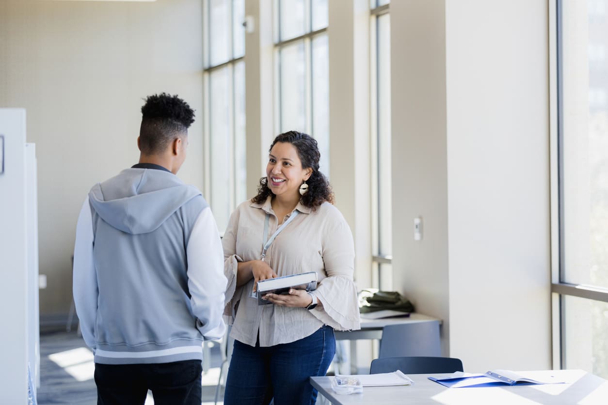 The librarian approaches the young adult man with a resource she found for his research paper.